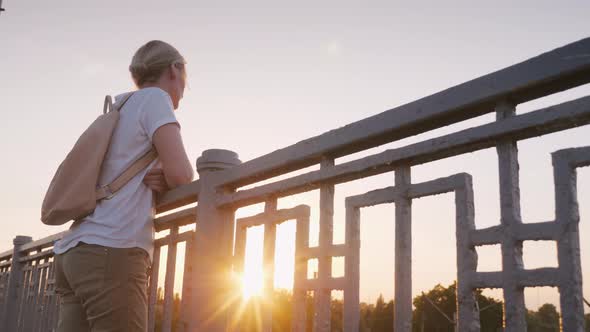 A Woman Stands at the Railing of the Bridge, Looking Into the Distance alt