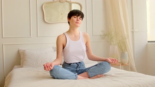 Young woman meditating while sitting on the bed at home in bedroom. alt