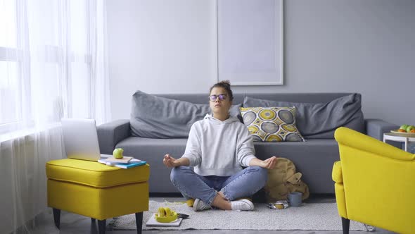 Young Woman in Glasses Meditates in Yoga Pose on Carpet