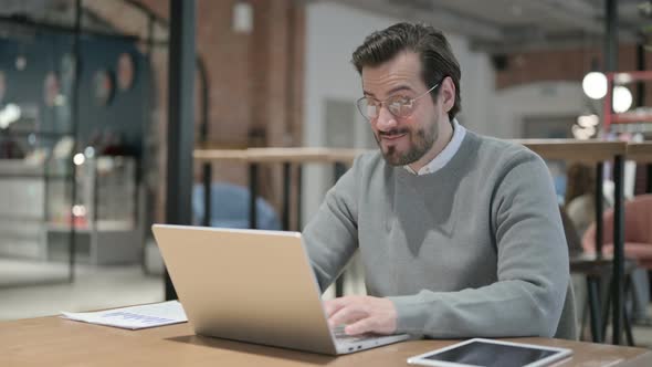 Young Man Celebrating Success While Using Laptop in Office alt