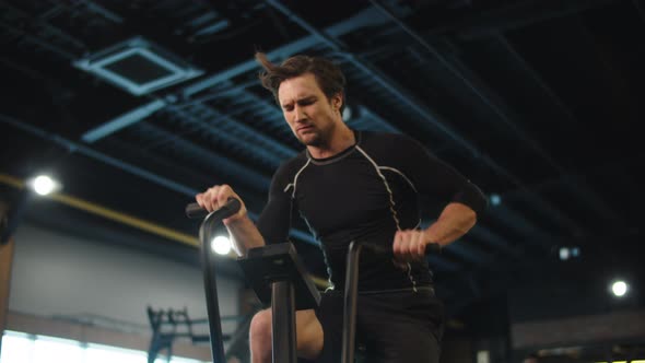 Angry Sport Man Doing Cardio at Gym. Fit Man Exercising on Velosimulator alt