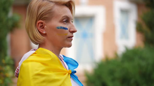 Side View Adult Woman in Embroidered Shirt and Ukrainian Flag Looking Away Standing on the Left alt