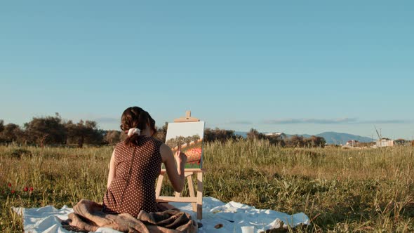 Young girl paints the picture on canvas in the countryside alt