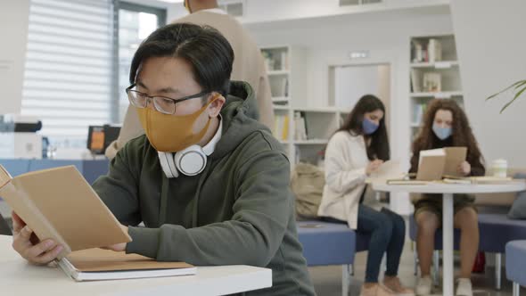 Asian Student Reading in Busy Library alt