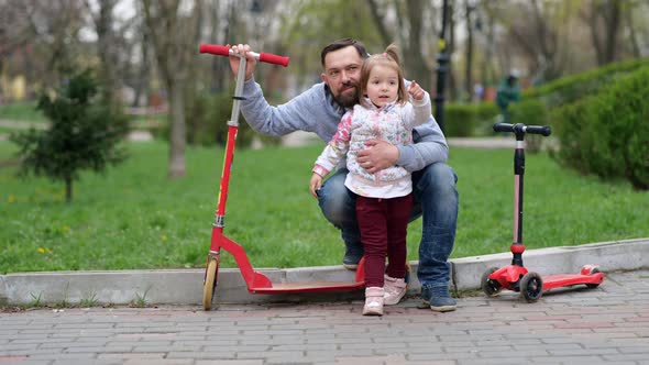 Happy Father and Little Daughter with Scooters in Park
