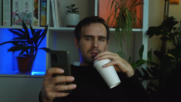 A man dressed in black drinks juice through a straw from a white paper cup