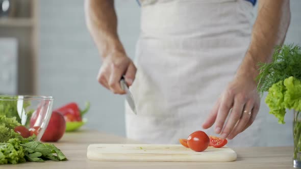 Man in Apron Carefully Cutting Tomatoes for Salad and Putting Them in Bowl alt