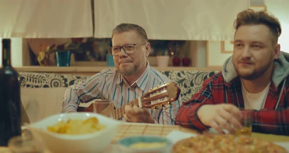 Company of Friends Communicates at Home. Man with Glasses Sings Songs with a Guitar. Friends Eat alt