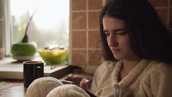 Teen Girl Playing in the Mobile Phone While Sitting in the Kitchen at Breakfast alt