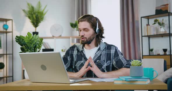 Office Worker in Headphones Holding Video Meeting with Coworkers from Home Office alt