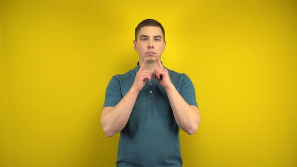 A Young Man Makes a Sad and Cheerful Smile on His Face with Her Fingers on a Yellow Background. Man alt