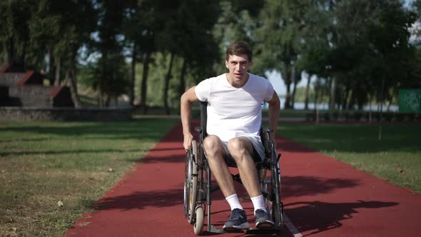 Smiling Man Rolling Wheelchair on Sports Field on Sunny Spring Summer Day alt