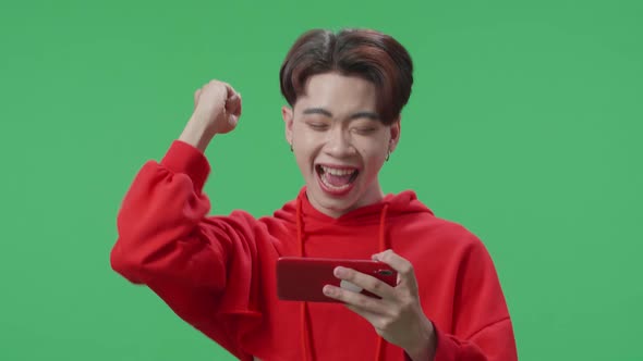 Transgender Male Celebrating After Winning Game On Mobile Phone While Standing In The Green Screen alt