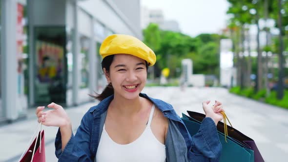 Smiling young Asian woman with shopping colour bags over mall alt