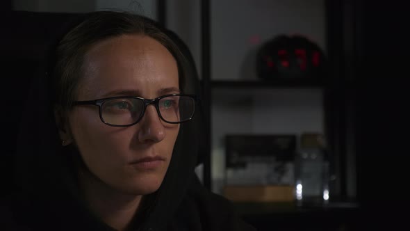 Young female programmer in eyeglasses is using laptop in dark, looking at computer screen.  alt