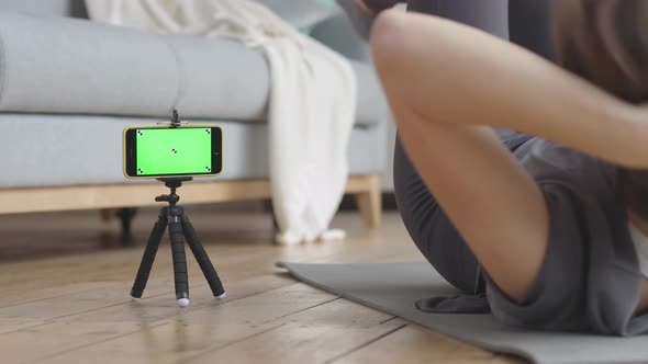 Young Woman Doing the Home Fitness Exercises. Green Screen and Marks on her Phone. alt