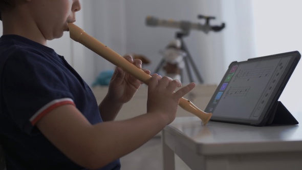 Niño pequeño practica flauta dulce con una App en su habitación.