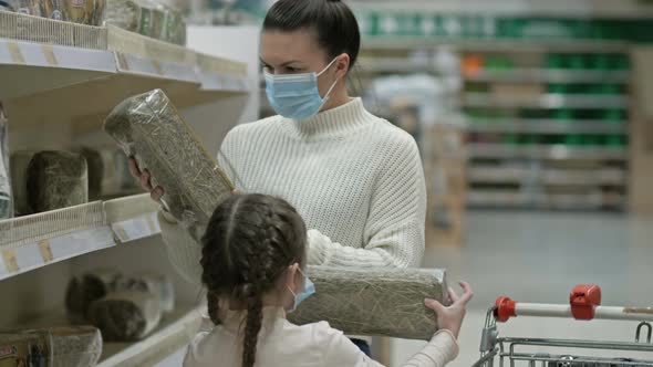 Mom and Daughter 67 Years Old Choose Hay for a Rabbit in the Pet Section of the Supermarket alt