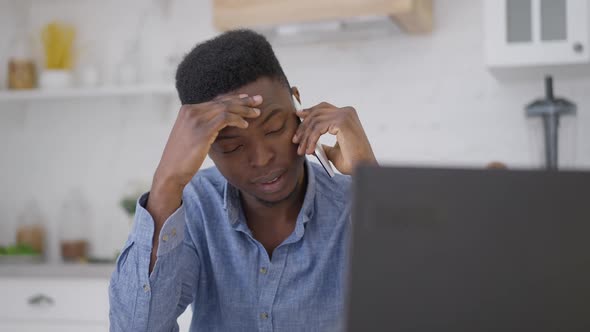 Portrait of Young Professional Man Rubbing Forehead Talking on the Phone in Home Office alt
