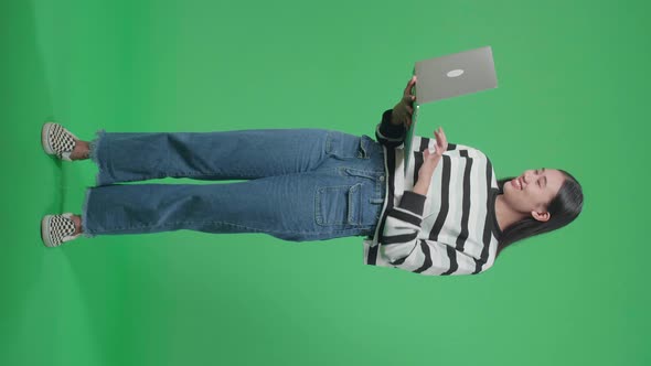 Full Body Of A Smiling Asian Woman Typing On Computer While Standing In Front Of Green Screen alt