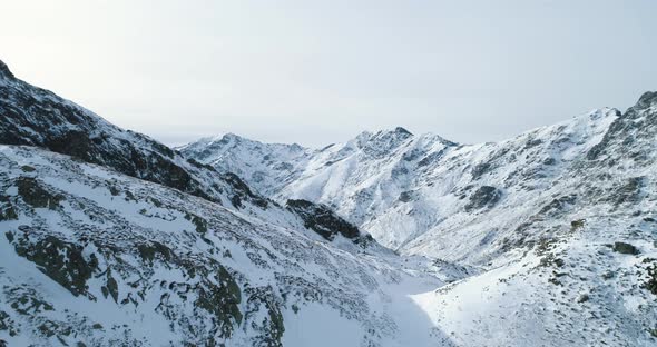 Backward Aerial Top View Over Winter Snowy Mountain Rock Peaks