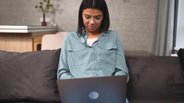 Smiling Multiracial Woman Wearing Domestic Clothes is Sitting in the Living Room with Laptop