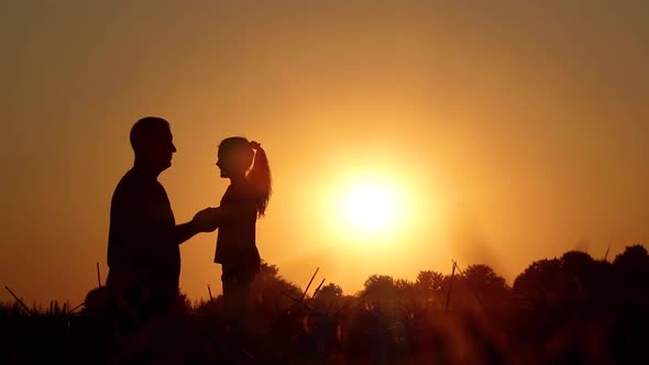 SLOW MOTION: Happy little daughter runs up to dad in the field at sunset. Silhouettes of people.