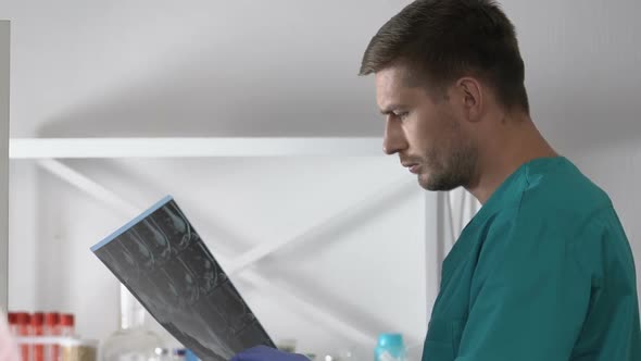 Doctor Studying Arm X-Ray, Sad Female Patient With Bandage Looking at Camera