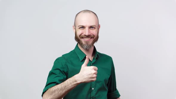 Happy bearded man in shirt showing thumbs sign up over white background. Good job