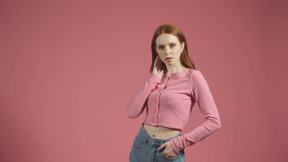 Serious Young Woman with Long Red Hair Poses for the Camera on an Isolated Pink Background