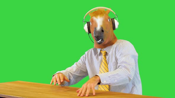 Chilling Man Wearing Wireless Headphones Sit at Table in Horse Mask Listening to Music and Dancing