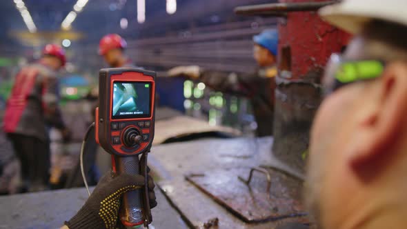 A Worker Uses a Video Camera to Inspect Equipment in a Factory alt