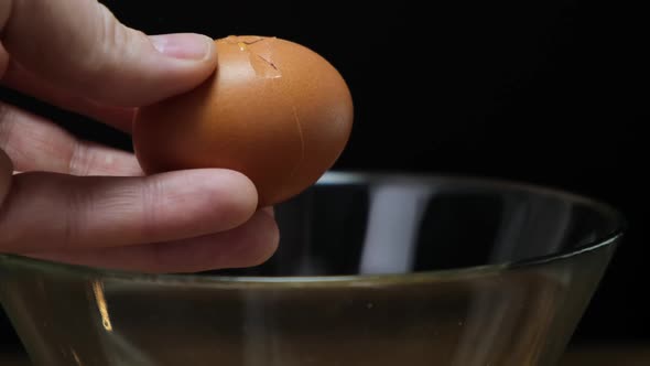 Hands holding one brown organic egg. Cracking over glass bowl. Close up. HD