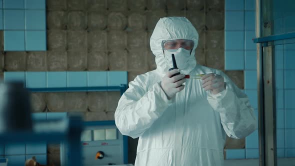 A medical worker in a protective suit and glasses holds a walkie-talkie in the hands