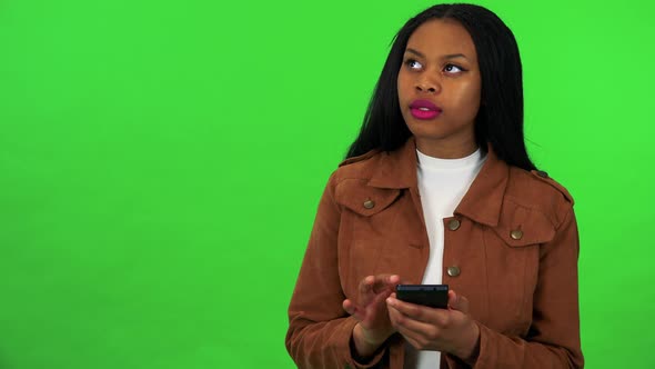 A Young Black Woman Works on a Smartphone with a Smile - Green Screen Studio alt