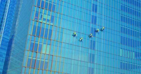 Five Men Workers in Red and Yellow Work Clothes Cleaning the Exterior Windows of a Business alt