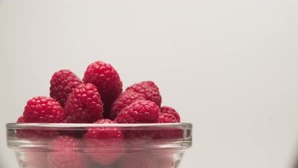 Close-up of a bowl of ripe scarlet raspberries on a white background.