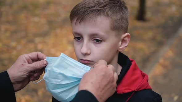 Grandmother Helps Puts a Medical Mask on the Face of Her Grandson