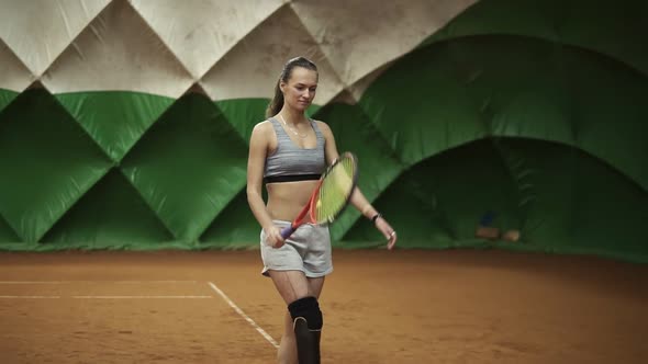 Young Long Haired Woman in Sportswear is Walking on the Indoor Tennis Court with Racket in Her Hand alt