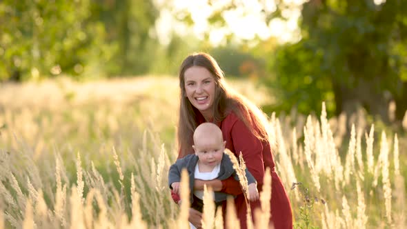 Young Loving mum and baby playing together outdoor enjoy beautiful sunset in the field. alt