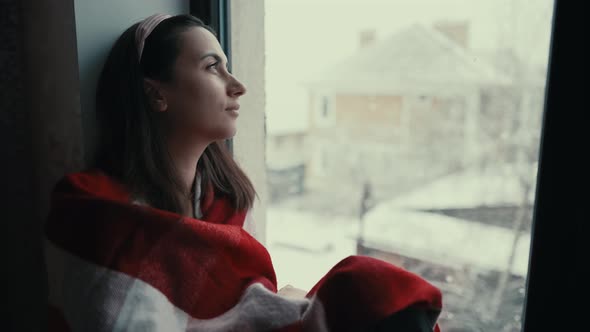 Sad Woman Looks Outside the Window Sitting on Windowsill alt