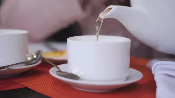 Close-up of Woman Pouring Hot Green Tea in a White Cup Standing on a Table in the Restaurant