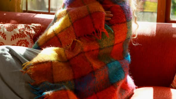 Mature woman wrapped in blanket at home alt