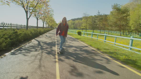 Skillful Woman Skater Riding Skateboard in Seated Position on Park Road alt