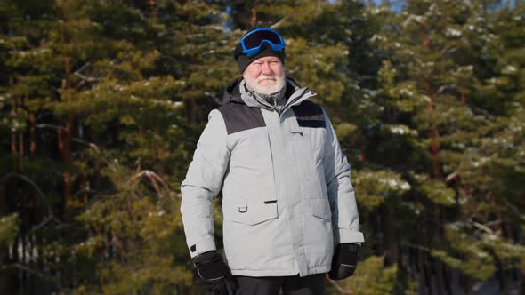 Portrait of Elderly Active Man in Warm Clothes and Ski Goggles Backdrop of Snowy Forest Smiling and