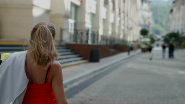 a Woman in Red Clothes Has Thrown Jacket Over Shoulder Turns and Walks Away Against the Background alt