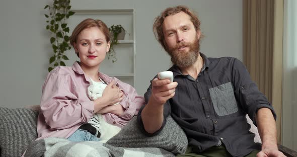 Young Caucasian Couple Watching TV Movie Program with Cat Pet Kitten Animal Relax Enjoying Rest at alt
