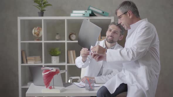 Two Male Doctors Checking X-ray in the Office of Modern Clinic. Men Reach Consensus and Shake Hands alt
