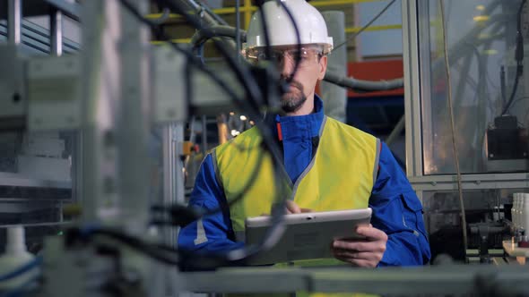 Man Types on a Tablet While Checking Factory Equipment, Automated Production alt