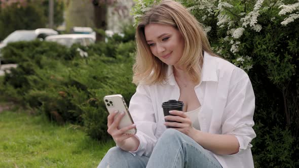 Beautiful Blonde Woman Uses Smartphone in the City Park